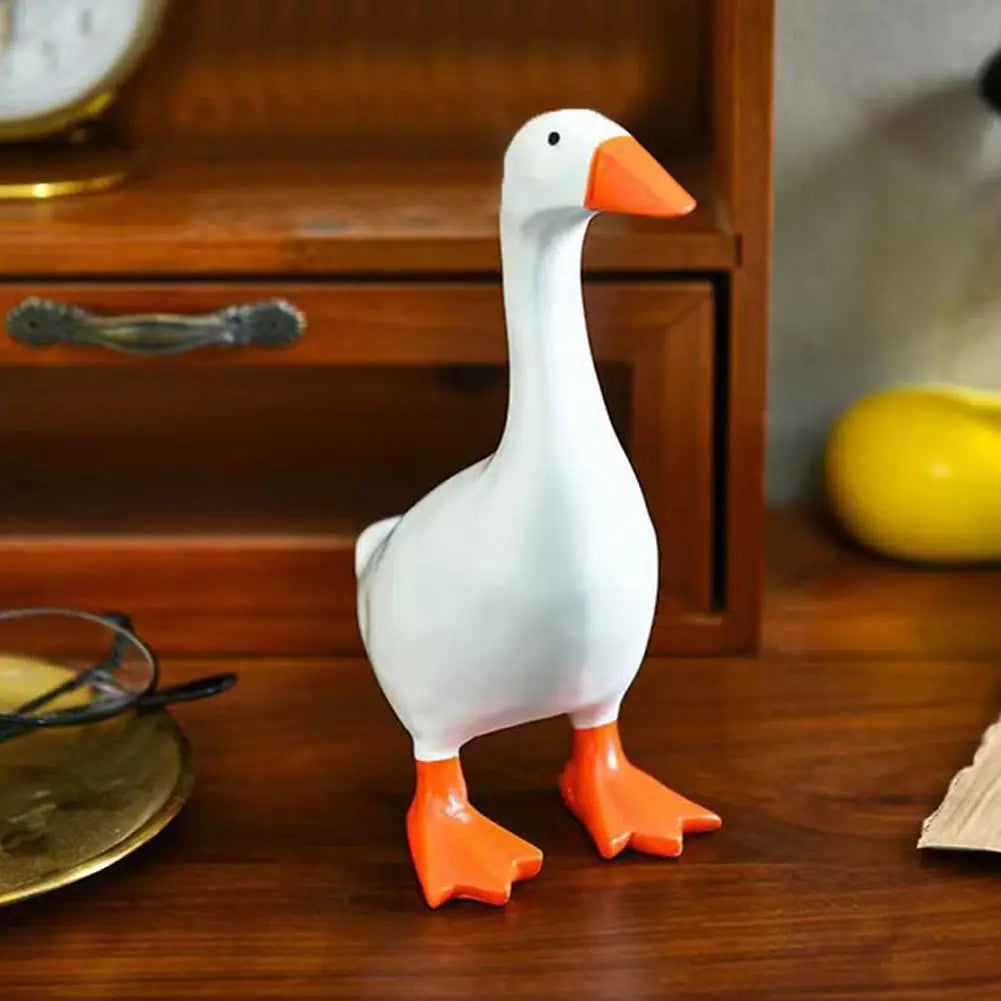 A white resin duck figurine with orange beak and feet, used as a desk organizer.