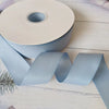 Roll of light blue matte finish satin ribbon lying on a white wooden surface.
