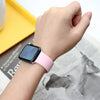 A hand wearing a pink silicone sport band on an Apple Watch, resting near a yellow box and printed paper.