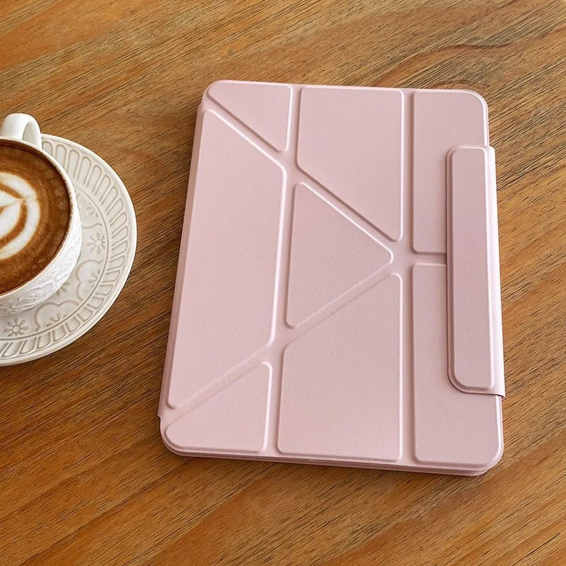 A pink magnetic protective case designed for an iPad Pro or iPad Air resting on a wooden surface next to a coffee cup.