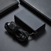 A black 100W USB-C PD laptop charger adapter with a coiled cable is shown on a dark surface.