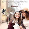 A woman is using a long selfie stick with a camera and fill light in an outdoor setting.