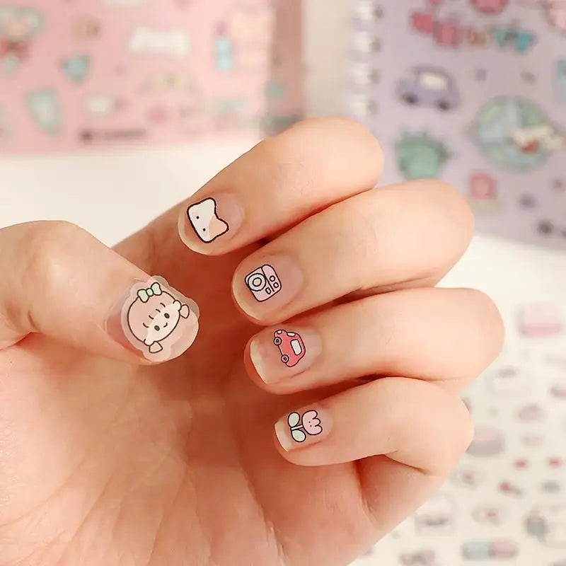 A hand displays fingernails decorated with small, cute cartoon stickers on a light pink background.