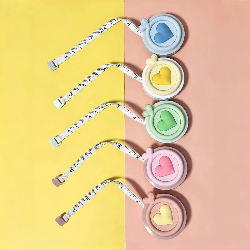Un juego de cintas métricas retráctiles en forma de corazón y colores pastel, incluyendo azul, amarillo, verde y rosa.