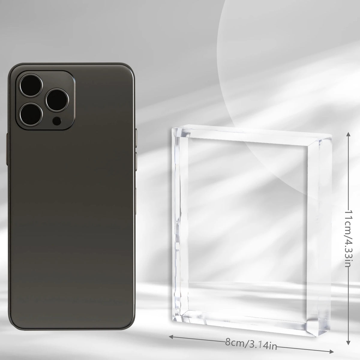 A dark gray smartphone next to a clear rectangular glass box, showing the dimensions of the box.