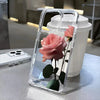 A clear phone case shaped like a pink rose is displayed on a table next to a white cup.
