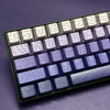 Vista cercana de un teclado mecánico con teclas gradientes en tonos morados y grises.