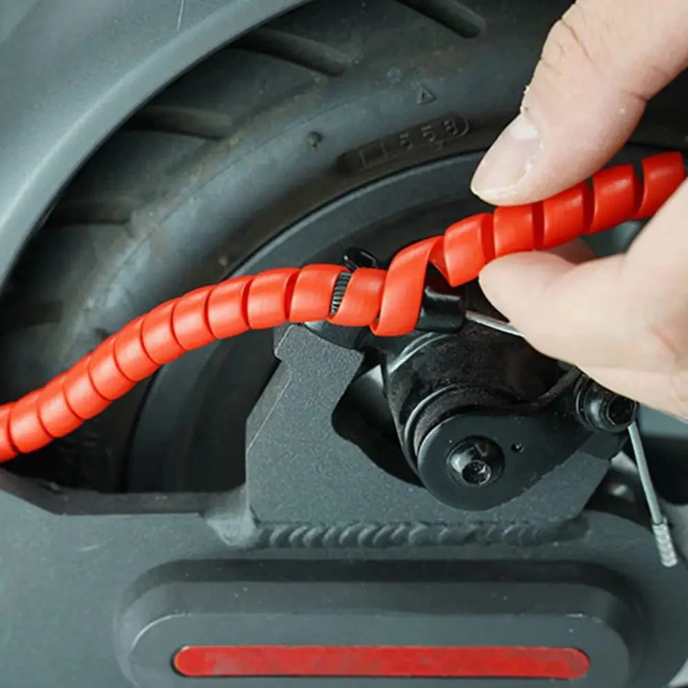 Une main tient un protecteur de câble orange pour scooter, près d'un composant moteur.