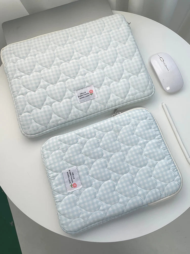 A light blue quilted laptop sleeve with a matching white wireless mouse is displayed on a white table.