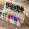 A clear acrylic 3-layer desk organizer holds various colored pens and pencils in individual slots.