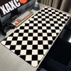 A black and white checkered desk mat is displayed on a desk next to a keyboard and gaming controller.