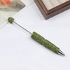A silver pen accessory with a green rhinestone bead tip and textured body is shown on a white surface.