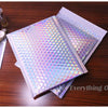 A stack of iridescent rainbow foil bubble mailers for gifts and documents resting on a wooden surface.