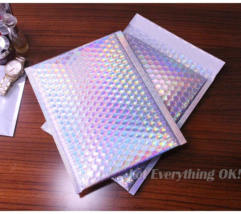 A stack of iridescent rainbow foil bubble mailers for gifts and documents resting on a wooden surface.