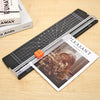 A portable manual paper trimmer with a black body and clear plastic blades is shown on a wooden surface.