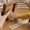 A hand applies hot melt glue sticks to a wooden photo frame for adhesion.