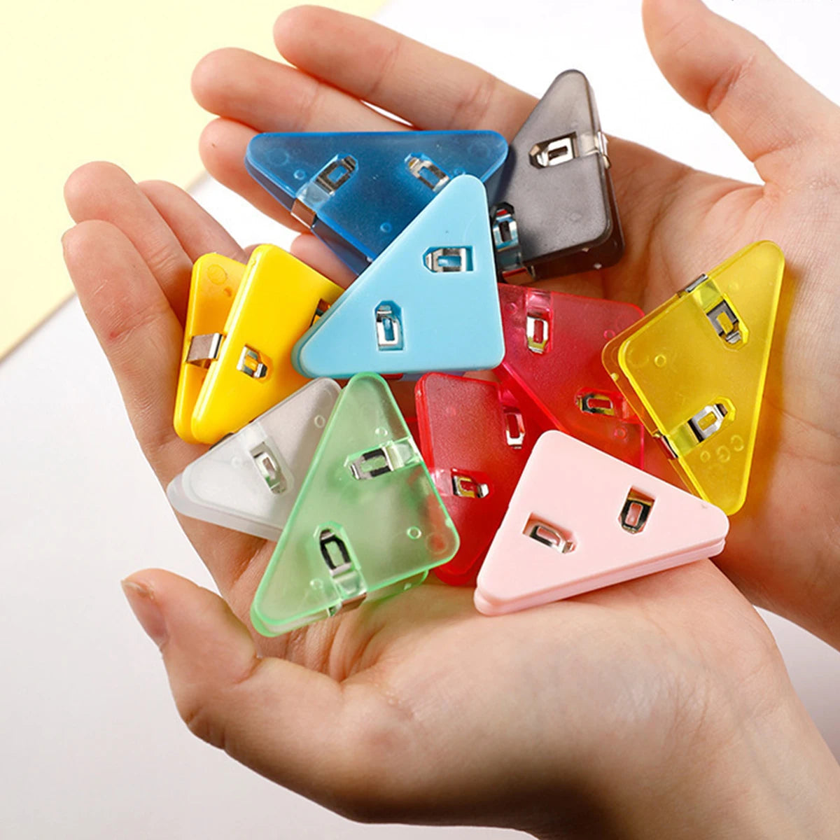 A hand holds several colorful triangle folder clips for documents.