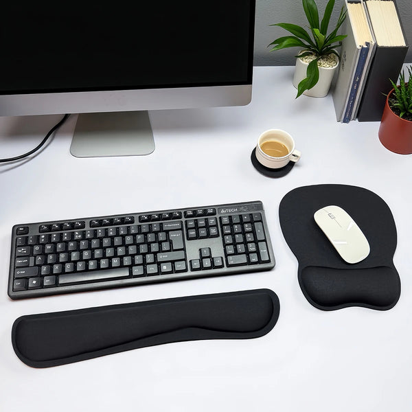 A set of black ergonomic keyboard wrist rest and mouse pad placed on a white desk next to a computer monitor.
