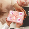 Eine Hand hält eine pinke Box mit Dankesaufklebern zum Scrapbooking mit einer pinken Schleife vor dunklem Hintergrund.