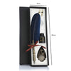 A black gift box containing a feather dip pen set with a dark blue feather, a gold nib, and a metal pen accessory.