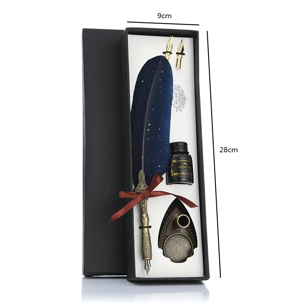 A black gift box containing a feather dip pen set with a dark blue feather, a gold nib, and a metal pen accessory.