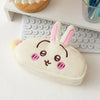 A cute pink and white Chiikawa plush pencil case shaped like a rabbit, resting on a white desk next to a keyboard.