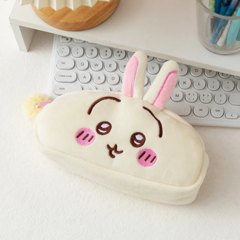 A cute pink and white Chiikawa plush pencil case shaped like a rabbit, resting on a white desk next to a keyboard.