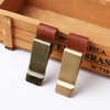 A pair of brass pen holders with brown leather straps resting on a wooden box.