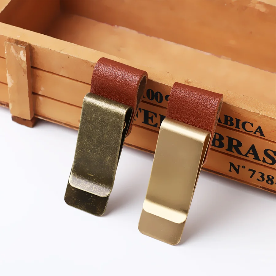 A pair of brass pen holders with brown leather straps resting on a wooden box.