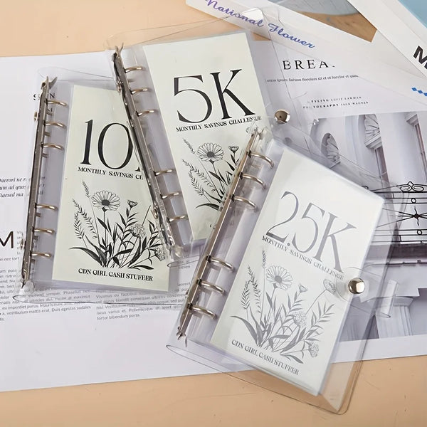 A set of three transparent binders showing monthly savings challenges for 5K, 10K, and 25K goals.