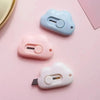 Three pastel colored utility knives shaped like rabbits with round buttons and blades displayed on a pink surface.