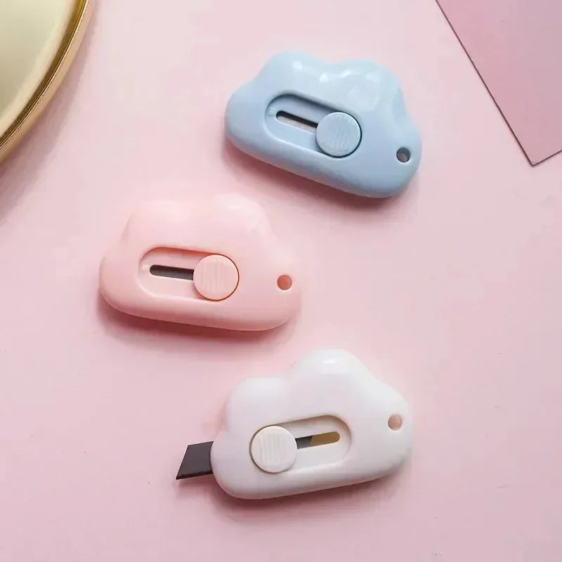 Three pastel colored utility knives shaped like rabbits with round buttons and blades displayed on a pink surface.