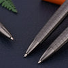 A close-up shot of a silver metal ballpoint pen resting on dark leather with a green leaf in the background.