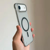 A hand holds a light gray slim magnetic phone case for an iPhone, featuring a circular design on the back.
