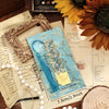 A vintage artistic metal bookmark with a blue tassel resting on aged paper.