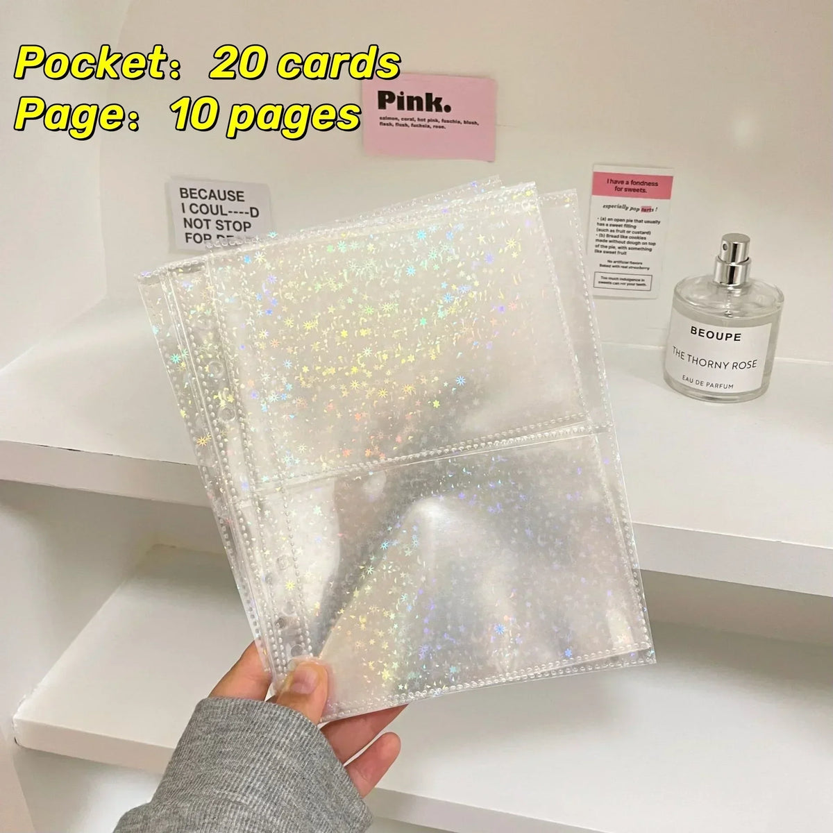 A clear, glittery A5 refillable photo sleeve is held against a white shelf with perfume bottles and paper.