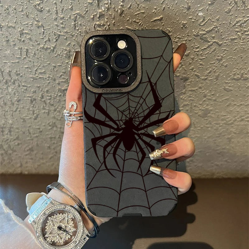 A hand holds a dark gray phone case featuring a black spider web design and a silver watch.