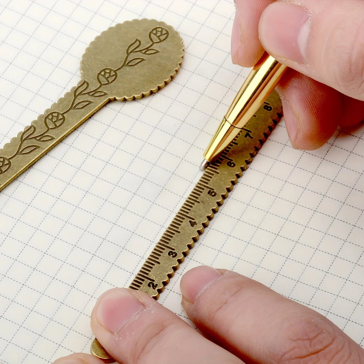 A hand holds a vintage brass straight ruler with a minimalist design placed on a graph paper background.