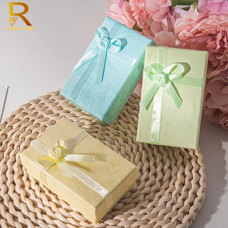 A set of two jewelry gift boxes, one light blue and one pale green, resting on a woven mat.
