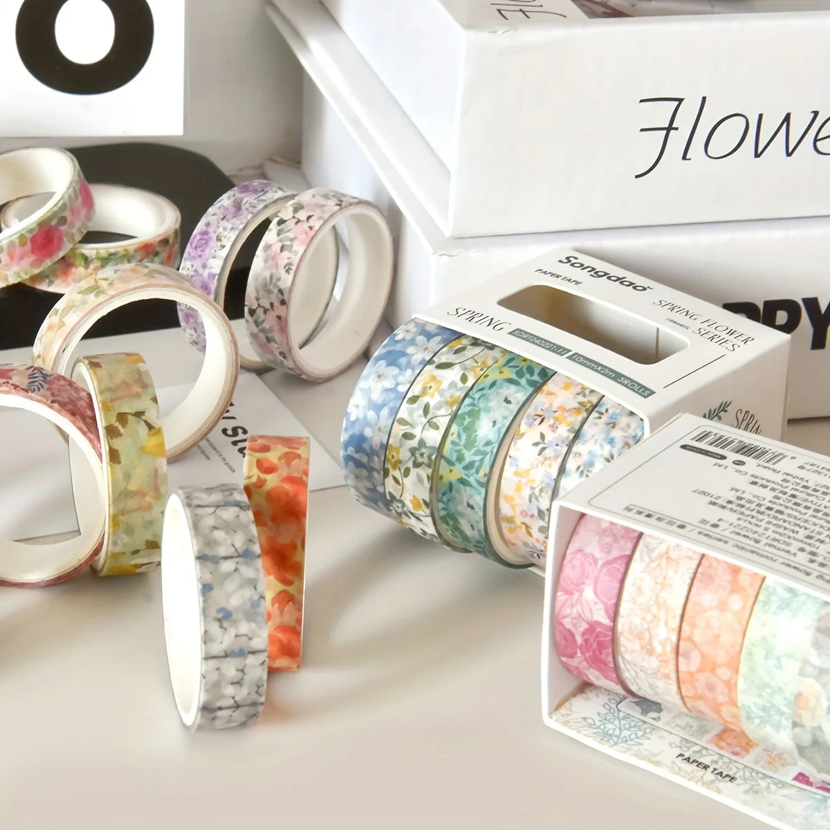 A collection of five rolls of floral patterned washi tape in various colors and designs displayed on a white surface.