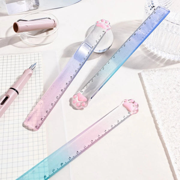 A pink and blue gradient measuring tool with cat paw shaped markings is shown next to a pen and a roll of tape.
