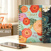 A spiral bound planner for 2027 with monthly and weekly planning pages displayed on a white desk.