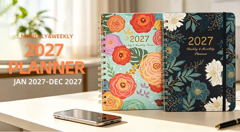 A spiral bound planner for 2027 with monthly and weekly planning pages displayed on a white desk.