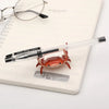 Un petit crabe fantaisiste rouge-orangé est posé sur un porte-stylo blanc.