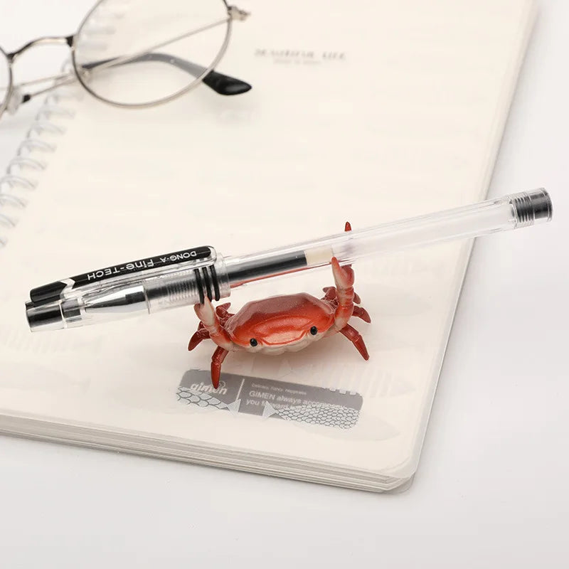 Un petit crabe fantaisiste rouge-orangé est posé sur un porte-stylo blanc.