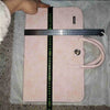 A pink laptop sleeve with a handle is shown lying on a gray fabric surface, measured by a ruler.