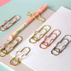 A collection of elegant gold and rose gold metal pen clips resting on a white notebook page.