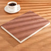 A brown notebook lies on a wooden surface next to a white cup and saucer.