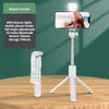 A white 3-in-1 selfie stick tripod with an LED light and Bluetooth remote is displayed on a wooden table.