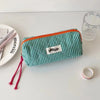 A green checkered pencil case with orange trim rests on a white surface next to a glass and a pink ribbon.